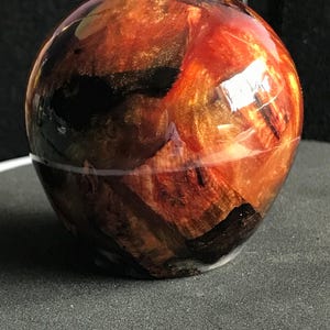 May include: A spherical decorative object with a glossy finish. It features a marbled effect with red, orange, gold, and black colours. The object is likely made of resin or a similar material.