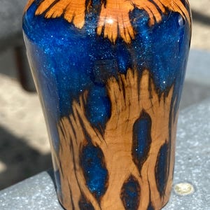 Könnte beinhalten: Ein zylindrischer Schaltknauf aus natürlichem hellbraunem Holz und durchscheinendem blauem Harz. Das Harz hat ein schimmerndes, glitzerndes Finish und ist durchgehend mit organischen Holzmaserungsmustern in der gesamten Struktur versehen.