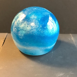 May include: A spherical, decorative object with a gradient of blue hues, from a deep azure at the top to a lighter, almost white shade at the base. The surface has a glittery, speckled effect, adding a shimmering quality to the design.