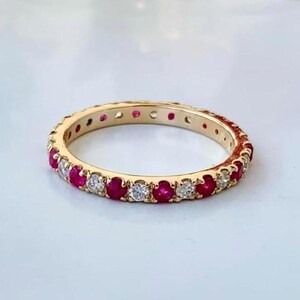 Könnte beinhalten: Ein goldener Eternity-Ring mit einem abwechselnden Muster aus runden roten Rubinen und klaren weißen Diamanten, die in einem durchgehenden Kreis gefasst sind. Der Metallring hat eine polierte Oberfläche, die die roten Edelsteine hervorhebt.