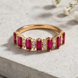 Könnte beinhalten: Ein Goldring mit einer Reihe abwechselnder, rechteckig im Baguetteschliff geschliffener roter Rubine und kleiner, runder, klarer Diamanten. Die Edelsteine sind in einem durchgehenden Muster auf der Vorderseite des polierten Goldrings gefasst.