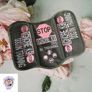 May include: A dark green dog training vest with pink details and white text. The vest says "STOP IGNORE K9 DOG IN TRAINING" and features icons. The vest is designed for dogs undergoing training.