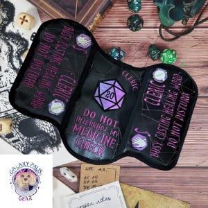 May include: Black, tri-fold dice bag with purple embroidered text and accents. The bag reads "Cleric, Busy Casting Healing Word, Do Not Disturb" and "Do Not Interrupt My Medicine Check". A purple D20 die is featured.