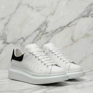 Zapatillas deportivas extragrandes de Alexander McQueen: Piel blanca, estilo urbano de lujo, tacón de ante negro.