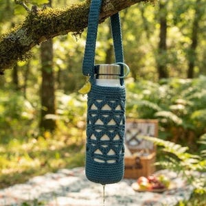 Può includere: Una borraccia bianca inserita in una custodia all'uncinetto color verde ottanio scuro con un motivo geometrico traforato e una lunga tracolla abbinata. Un piccolo ciondolo giallo a forma di limone pende dalla tracolla vicino al tappo metallico.