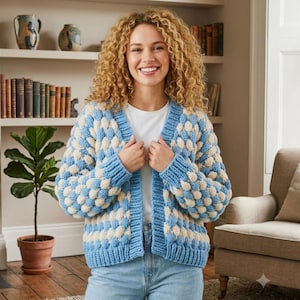 May include: A chunky knit cardigan featuring a repeating bobble stitch pattern in alternating light blue and cream colors. The garment has a V-neckline, long sleeves, and ribbed trim along the front opening, cuffs, and hem, worn over a white shirt.