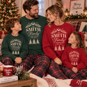May include: Matching family sweatshirts in dark green and red featuring a white graphic print that reads THE SMITH Family CHRISTMAS EST. 2026, surrounded by a decorative wreath of pine branches and three pine trees at the bottom of the design.