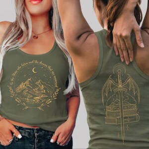 May include: Olive green tank top with a gold graphic on the front featuring mountains, a crescent moon, and text. The back of the tank top has a gold graphic of a sword, wings, and books. The tank top is worn by a person.