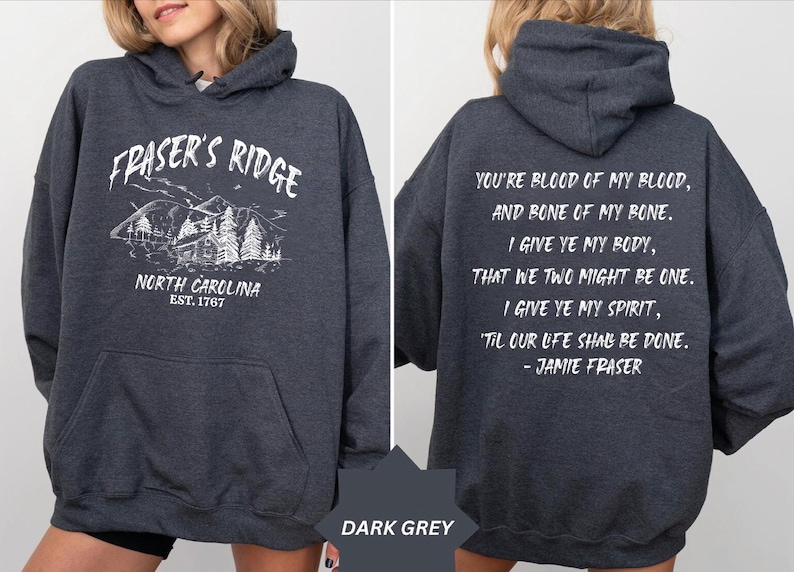 May include: A dark grey hooded sweatshirt featuring a white graphic on the front with the text Fraser's Ridge, North Carolina, Est. 1767 and a mountain cabin illustration. The back displays the white text You're blood of my blood, and bone of my bone.