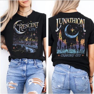 May include: A black short-sleeve t-shirt featuring a graphic print of a city skyline, a crescent moon, and stars. The front displays the text Crescent City and Light it up. The back features the text Lunathion and Crescent City.