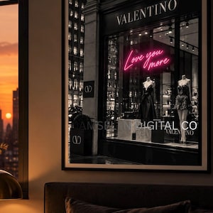 May include: A framed wall art print depicting a Valentino storefront at night. The window display features two mannequins in black dresses and a bright pink neon sign that reads Love you more. The storefront exterior is black with white text.