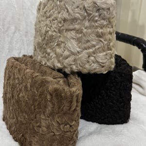 Puede incluir: Tres sombreros cilíndricos hechos de material de piel sintética texturizada y rizada. Los sombreros están dispuestos en un grupo, con un sombrero beige claro en la parte superior, uno marrón medio a la izquierda y uno negro a la derecha.