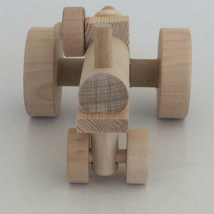 K&ouml;nnte beinhalten: Ein h&ouml;lzerner Spielzeugtraktor mit vier R&auml;dern, einem Schornstein und einem einfachen Design. Der Traktor ist aus unbehandeltem Holz.