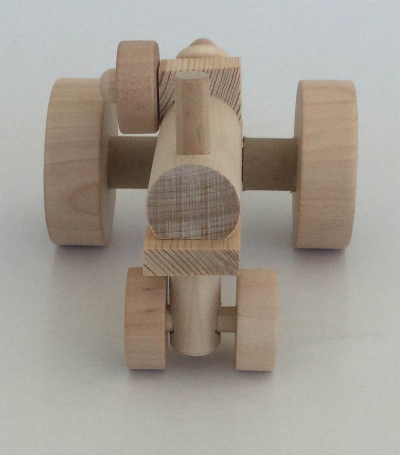 K&ouml;nnte beinhalten: Ein h&ouml;lzerner Spielzeugtraktor mit vier R&auml;dern, einem Schornstein und einem einfachen Design. Der Traktor ist aus unbehandeltem Holz.