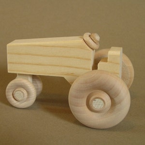 Op de afbeelding: Een houten speelgoedtractor met vier wielen, een cabine en een eenvoudig ontwerp. De tractor is gemaakt van licht hout en heeft een natuurlijke afwerking.
