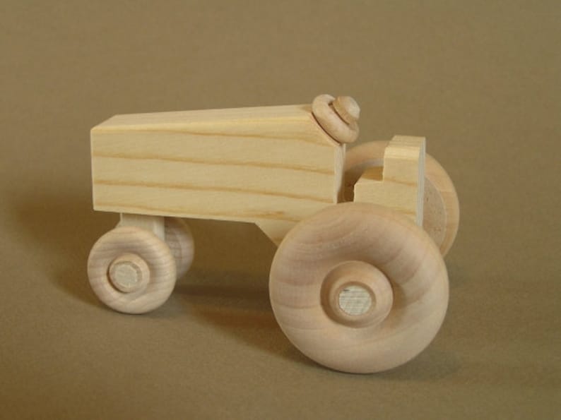 Op de afbeelding: Een houten speelgoedtractor met vier wielen, een cabine en een eenvoudig ontwerp. De tractor is gemaakt van licht hout en heeft een natuurlijke afwerking.