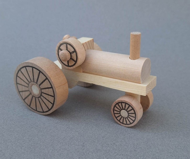 K&ouml;nnte beinhalten: Ein h&ouml;lzerner Spielzeugtraktor mit braunem K&ouml;rper, schwarzen R&auml;dern und einem schwarzen Schornstein. Der Traktor hat ein detailliertes Design auf den R&auml;dern.