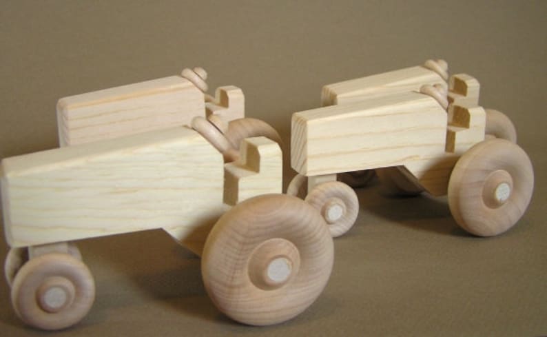 Op de afbeelding: Drie houten speelgoedtractoren, elk met een andere maat en vorm. De tractoren zijn gemaakt van natuurlijk hout en hebben een eenvoudig, rustiek ontwerp.
