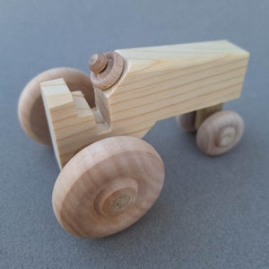 Op de afbeelding: Een houten speelgoedtractor met een lichtbruine afwerking. De tractor heeft vier wielen en een eenvoudig ontwerp.