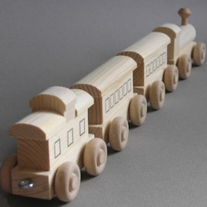 May include: A wooden toy train set with an engine and four cars. The train is made of natural wood and has black painted windows. The train is on a gray surface.