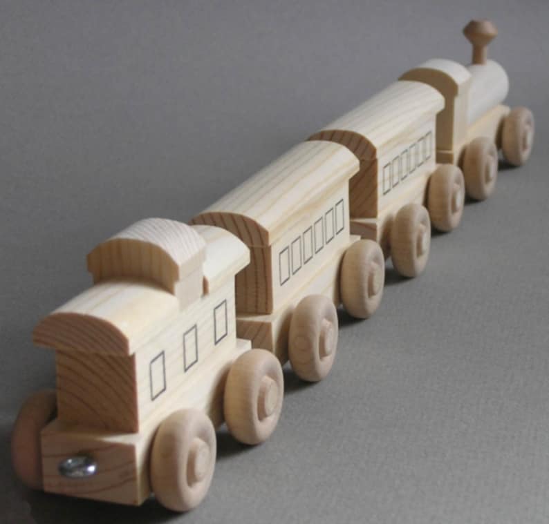 May include: A wooden toy train set with an engine and four cars. The train is made of natural wood and has black painted windows. The train is on a gray surface.