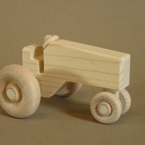 Op de afbeelding: Een houten speelgoedtractor met vier wielen. De tractor is gemaakt van onbehandeld hout en heeft een eenvoudig ontwerp.