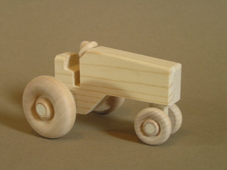 Op de afbeelding: Een houten speelgoedtractor met vier wielen. De tractor is gemaakt van onbehandeld hout en heeft een eenvoudig ontwerp.