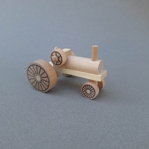 K&ouml;nnte beinhalten: Ein h&ouml;lzerner Spielzeugtraktor mit brauner Oberfl&auml;che. Der Traktor hat vier R&auml;der mit schwarzen Speichen und einen schwarzen Schornstein.