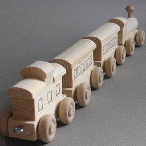 May include: A wooden toy train set with a locomotive and several passenger cars. The train is made of natural wood and has black painted details. The train is on a gray surface.