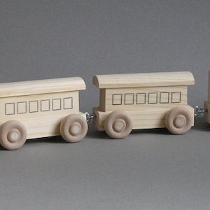 May include: A wooden toy train set with an engine, a boxcar, and a caboose. The train is made of natural wood and has black painted details.