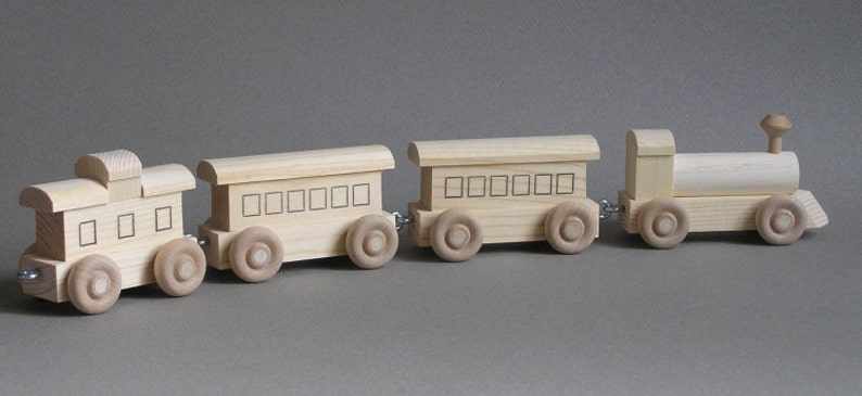 May include: A wooden toy train set with an engine, a boxcar, and a caboose. The train is made of natural wood and has black painted details.