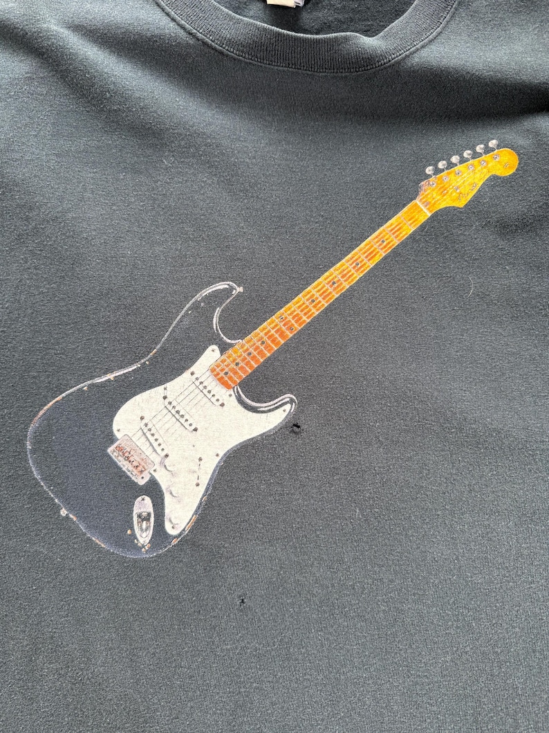 Pu&ograve; includere: Felpa nera con grafica di una chitarra elettrica vintage. La chitarra ha un corpo nero, battipenna bianco e manico e paletta gialli. La felpa &egrave; realizzata in un tessuto morbido e scuro.