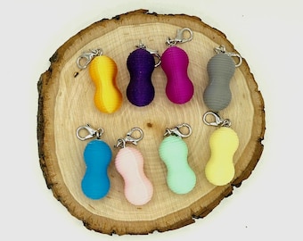 May include: A collection of eight peanut-shaped keychains in various solid colors including yellow, purple, magenta, gray, blue, light pink, mint green, and pale yellow. Each keychain features a silver-toned metal lobster clasp attachment.
