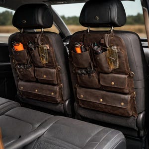 May include: Brown leather car seat organizers with multiple pockets and compartments. Each organizer hangs from the headrest and features various sized pockets, holding items like water bottles and tools. The organizers are designed to keep car interiors tidy.
