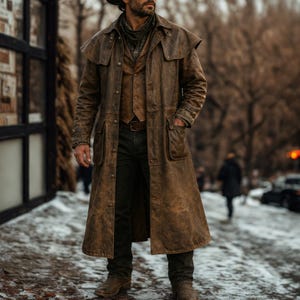 May include: A long, distressed brown leather duster coat featuring a wide collar, button-front closure, and two large patch pockets. Underneath, a brown button-up vest is worn over a dark shirt, paired with dark trousers and brown leather boots.