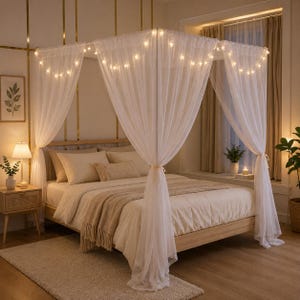 May include: A canopy bed with sheer white curtains and string lights. The bed has a light-colored wooden frame and is made up with neutral-toned bedding. A small side table with a lamp and a framed botanical print are visible.
