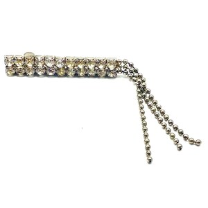 Può includere: Una molletta per capelli color argento con due file parallele di strass trasparenti, sfaccettati e dal taglio rotondo, incastonati nel metallo. Tre delicate catenelle a palline color argento pendono da un'estremità della molletta.