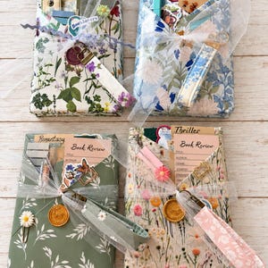 May include: Four rectangular packages wrapped in floral paper, each tied with white tulle ribbon and a fabric wristlet. Each package includes a Book Review card, a wax seal, and various stationery items like stickers, paper clips, and bookmarks.