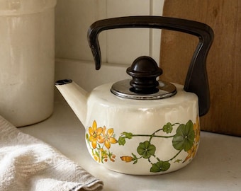 Tetera de esmalte vintage con estampado floral de enredaderas, color crema, con asa marrón, estilo rústico.