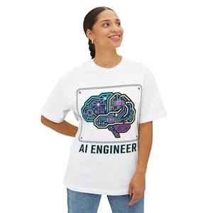 May include: White t-shirt featuring a graphic of a brain rendered as a circuit board in teal, pink, and purple. The text "AI ENGINEER" is below the graphic. The design is framed by a white rectangle with rounded corners.