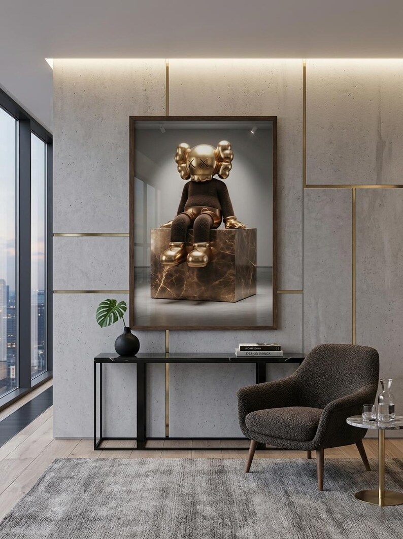 May include: A framed wall art print featuring a golden KAWS character with X-shaped eyes sitting on a brown marble cube. The figure has a brown torso, golden hands, and golden shoes, displayed in a modern room with a dark console and armchair.