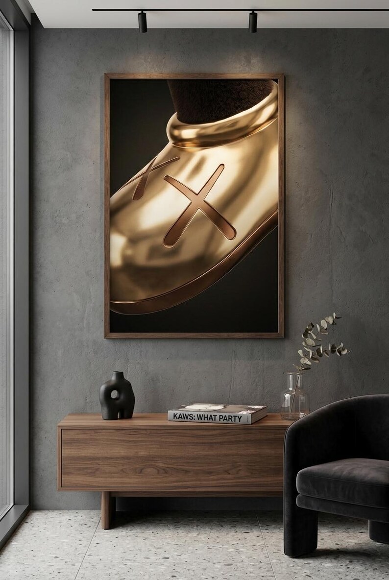 May include: A framed wall art print featuring a close-up of a shiny gold-toned shoe with a prominent X symbol on the side. The artwork is displayed in a dark wood frame, showcasing a smooth, reflective metallic surface against a dark background.
