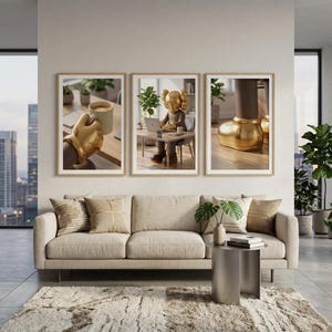 May include: Three framed art prints featuring a gold-colored sculpture in different settings. The prints are displayed above a beige sofa in a modern living room setting. The room has large windows and potted plants.