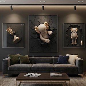 May include: Three framed wall art pieces featuring abstract figures emerging from cracked surfaces. The figures have gold accents. A gray sofa with decorative pillows and a wooden coffee table complete the living room setting.