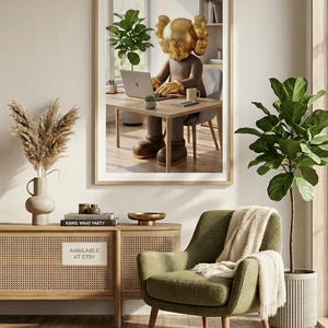 May include: A framed print featuring a KAWS figure with a gold head and gloves, working on a laptop at a wooden desk. The room includes a green armchair, a woven cabinet, and a potted plant. The text "AVAILABLE AT ETSY" is visible.