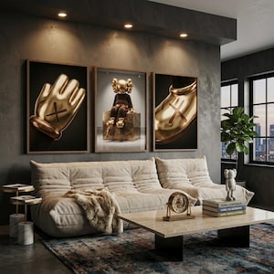 May include: Three framed wall art prints featuring gold-toned KAWS-style figures, including a close-up of a hand, a seated character on a block, and a shoe. The artwork is displayed above a beige tufted sofa with a faux fur throw and a marble coffee table.