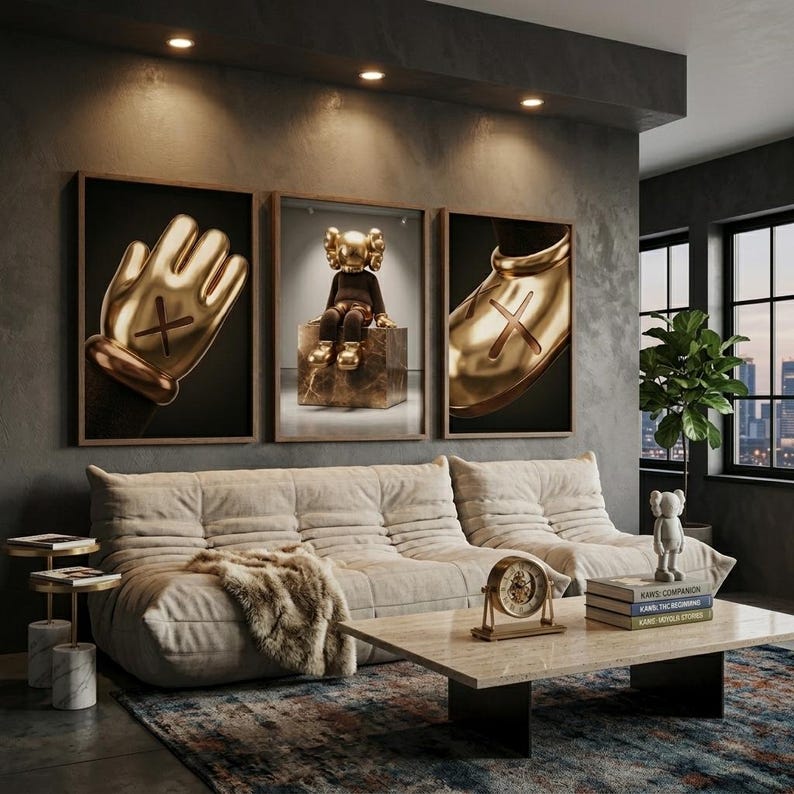 May include: Three framed wall art prints featuring gold-toned KAWS-style figures, including a close-up of a hand, a seated character on a block, and a shoe. The artwork is displayed above a beige tufted sofa with a faux fur throw and a marble coffee table.