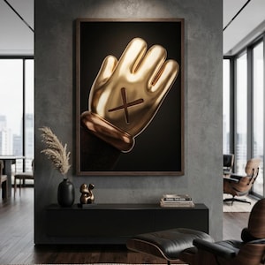 May include: A framed wall art piece featuring a glossy, metallic gold cartoon-style hand with a dark brown cuff and a prominent dark brown X symbol on the palm, set against a solid black background within a thin, dark wooden frame.