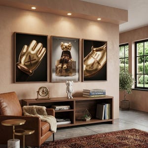 May include: Three framed wall art prints featuring gold-colored cartoon-style hands and a seated figure with X-shaped eyes. Below, a white figurine stands on a wooden console table next to a gold clock and a stack of books titled KAWS.