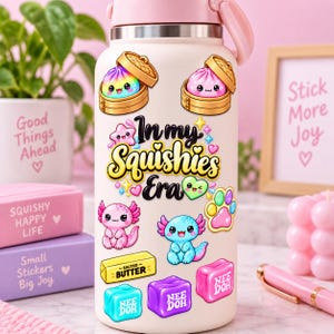 May include: A light pink insulated water bottle covered in colorful stickers featuring two rainbow and pink dumplings in bamboo steamers, a pink star, a green heart, a paw print, two axolotls, a stick of salted butter, and three Nee Doh cubes.